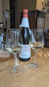 Eine Flasche Pinot Grigio steht auf einem Holztisch, davor 2 Gläser im Restaurant Olea Leipzig